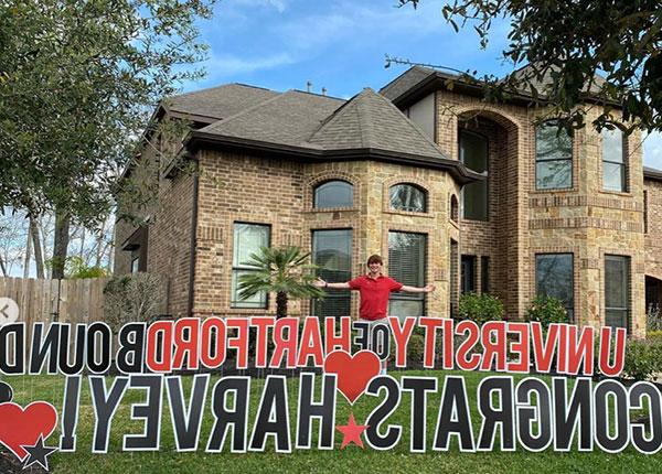 Accepted Student in front of home, with sign University of Hartford bound